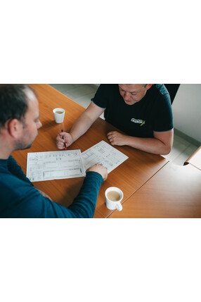 Twee mannen bespreken een project aan een bureau met koffie.